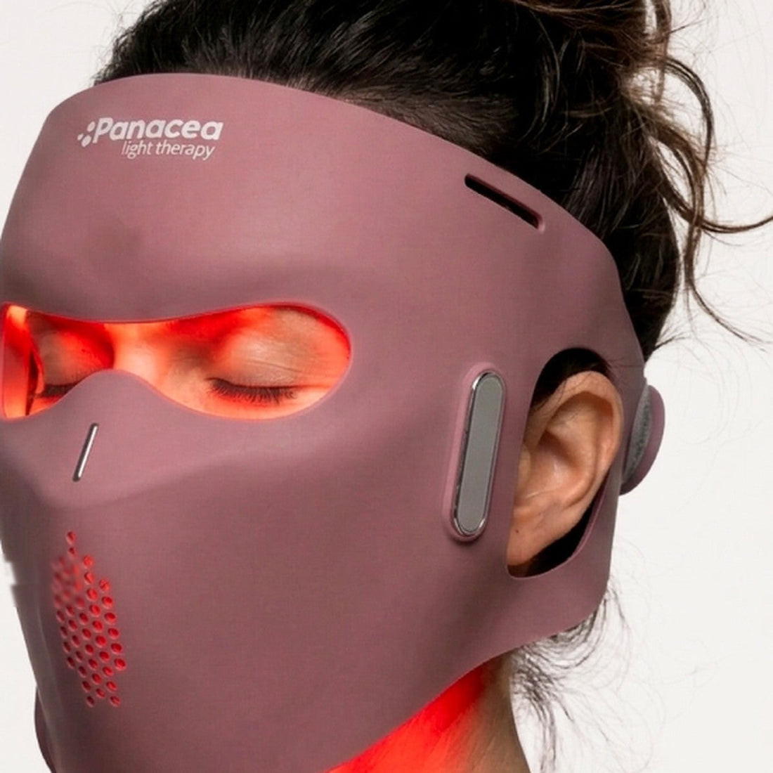 Vrouw met gesloten ogen draagt het bordeauxrode Aurora LED-gezichtsmasker, rood licht schijnt door de oogopeningen