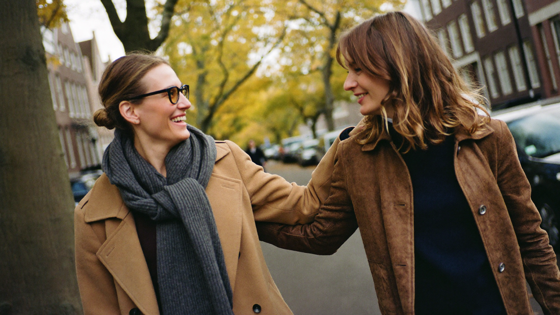 Twee vrouwen lopen arm in arm en lachend door een Nederlandse straat in herfstlicht