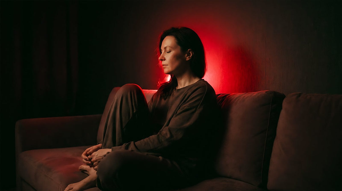 Frau sitzt abends auf dem Sofa im roten Licht eines Panacea-Panels